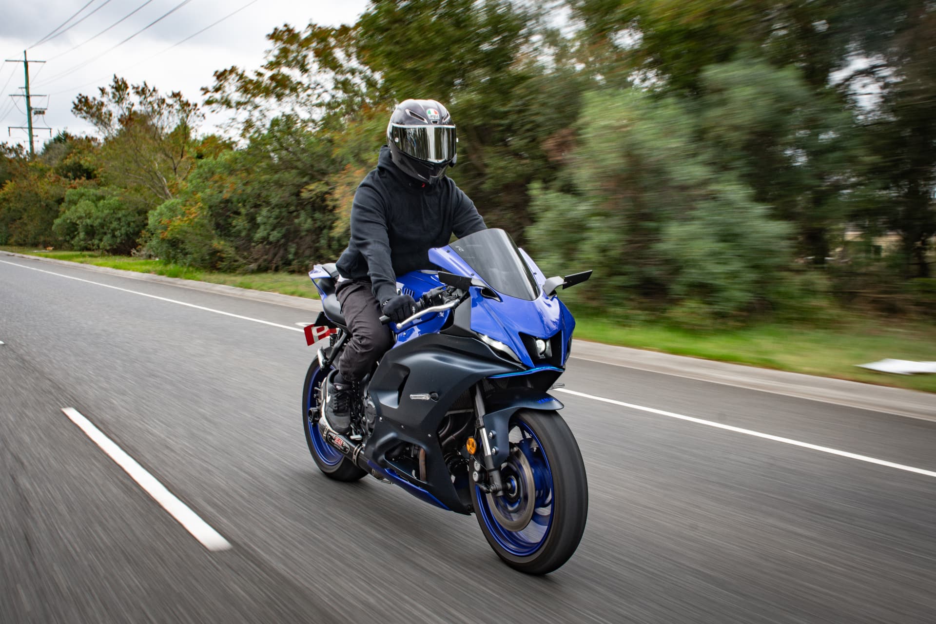 Motorcyclist riding a blue motorcycle on a tree-lined road