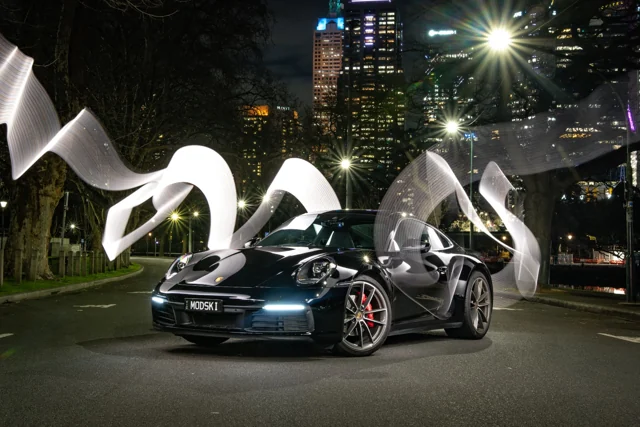 Dark sports car beneath illuminated city sculptures at night