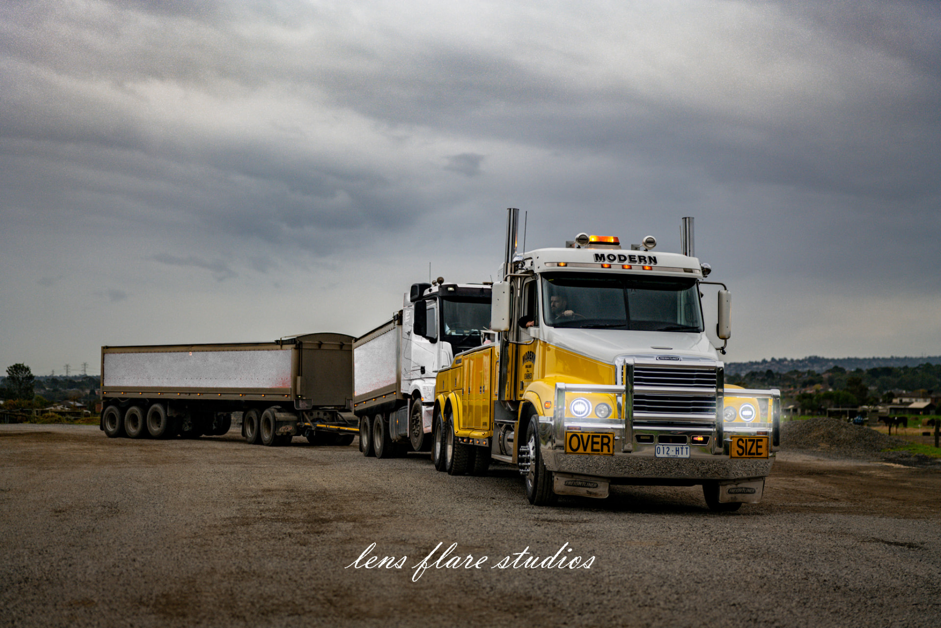 White and yellow truck with a trailer beneath an overcast sky