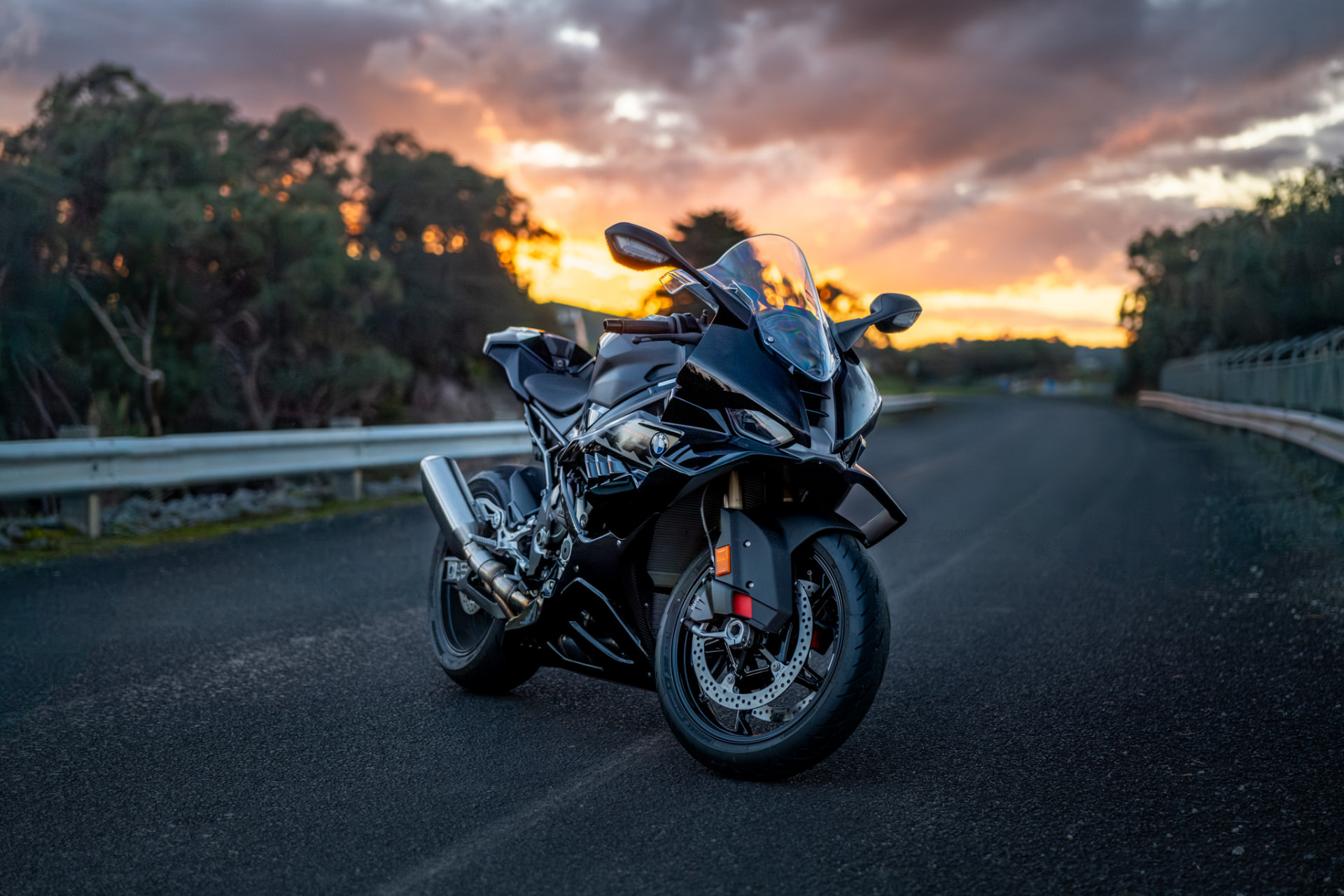 Motorcycle parked beside a guardrail at sunset