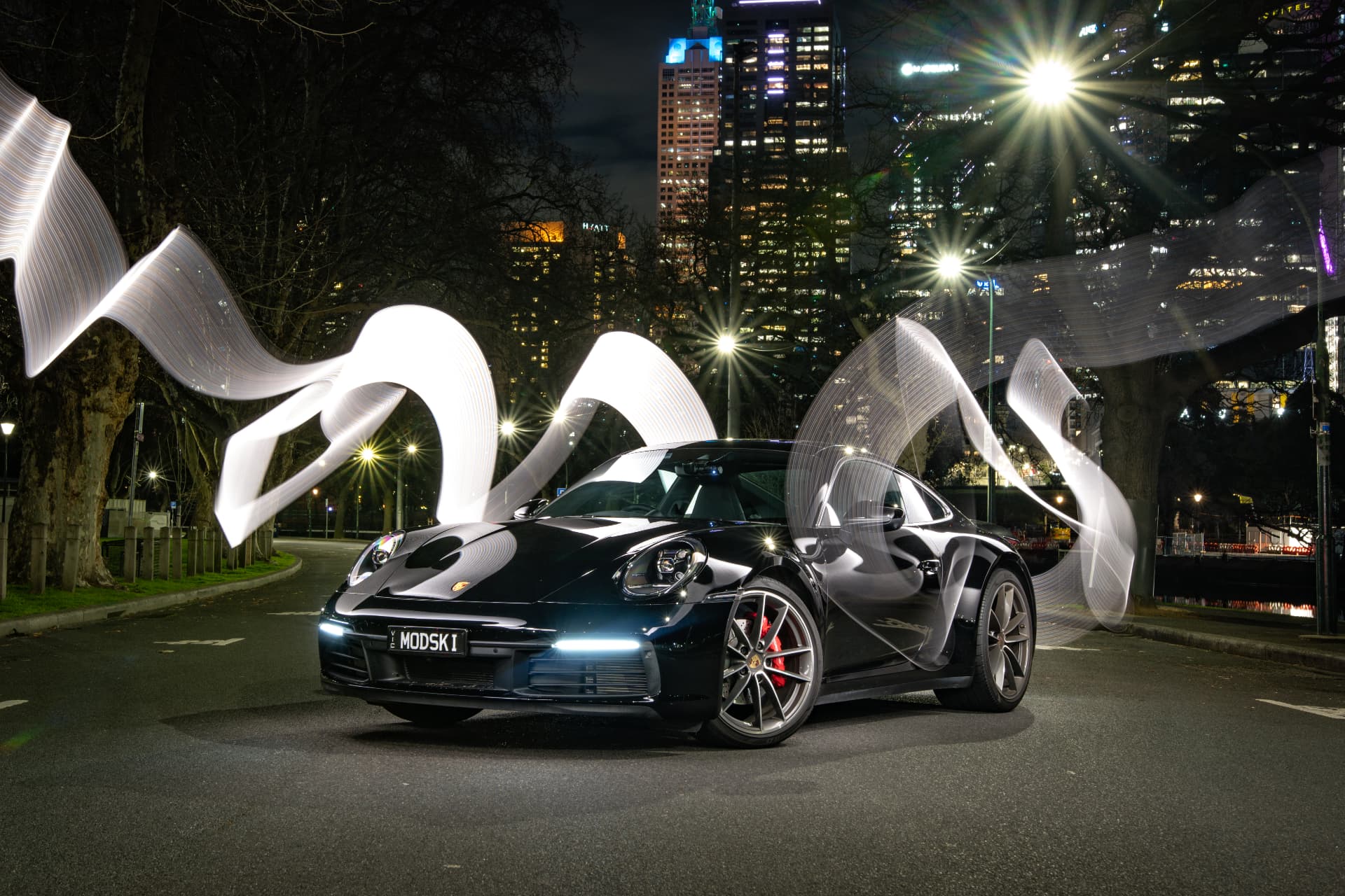 Dark sports car beneath illuminated city sculptures at night